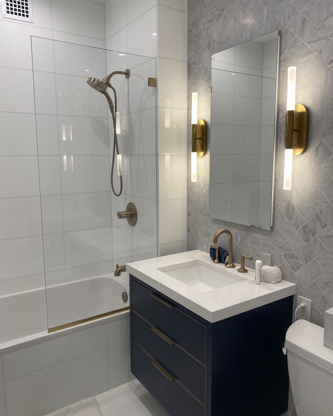 Navy vanity with brass sconces and glass tub screen